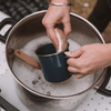 Person cleaning a blue mug with an eco scrub sponge in a pot of soapy water