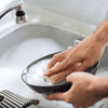 Person washing a frying pan with a sponge in a sink