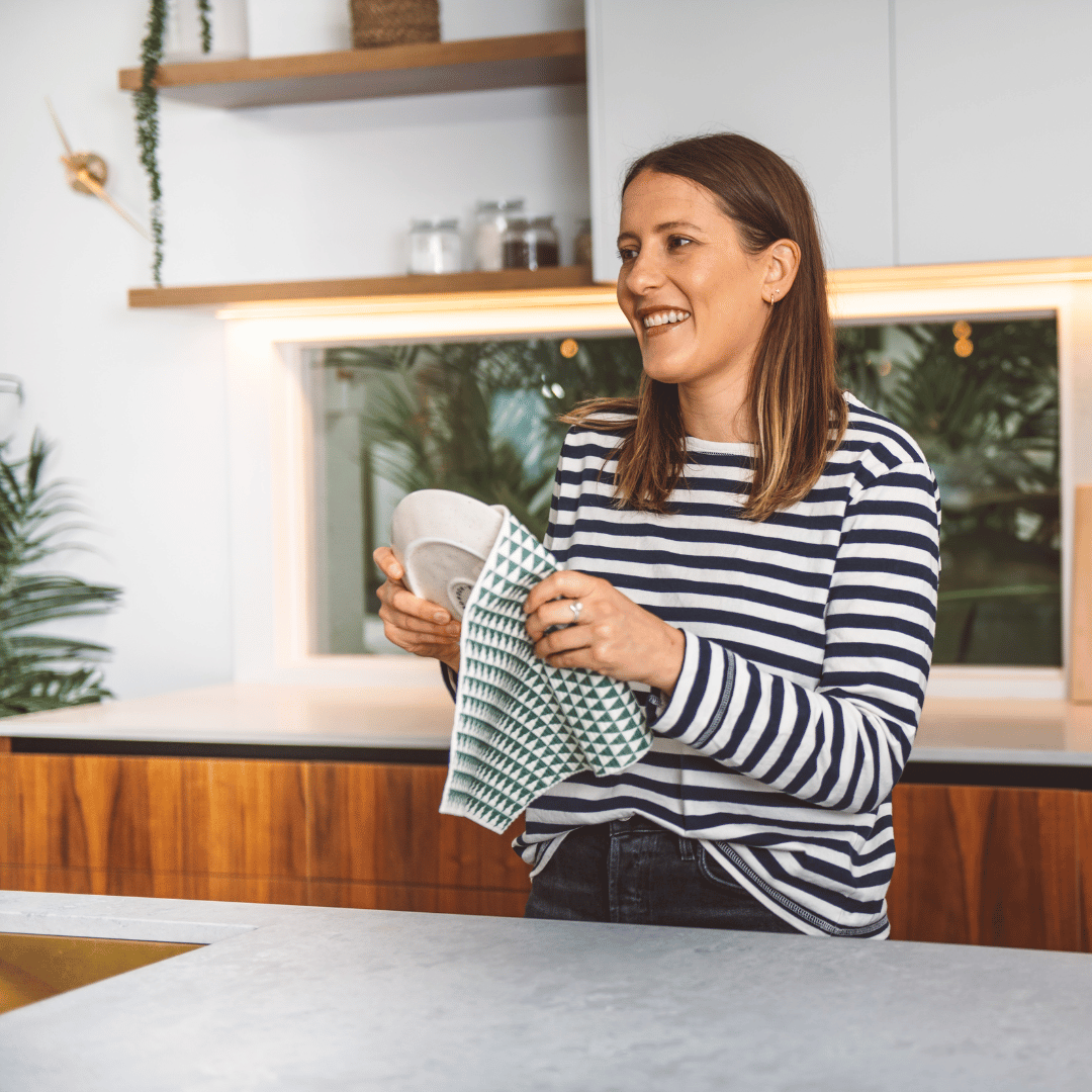 Woman holding a large eco cloth with green and white pattern, drying a plate, standing in a kitchen