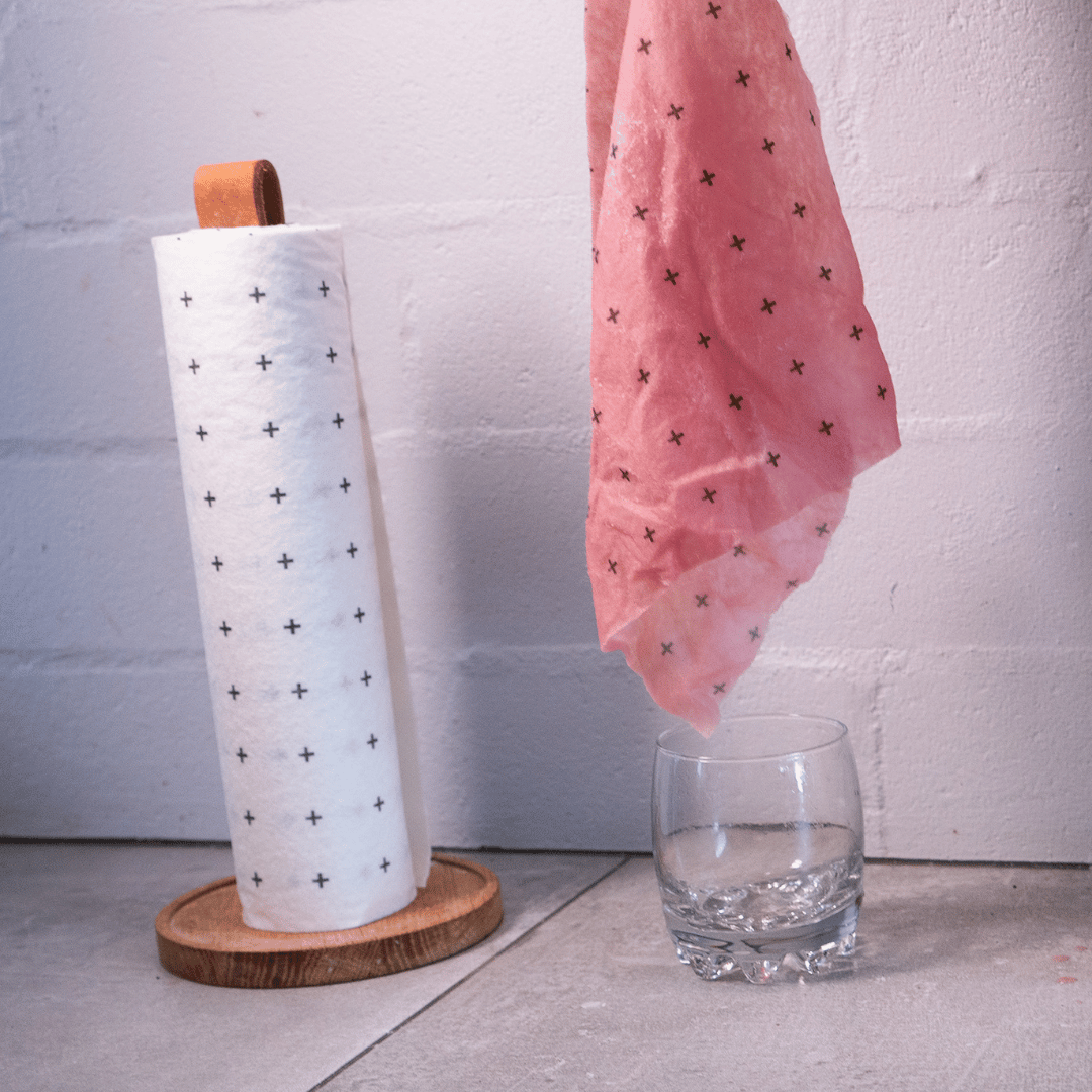 Roll of paper towels on a wooden stand, showing how much absorbency the bamboo towel has with an empty cup below