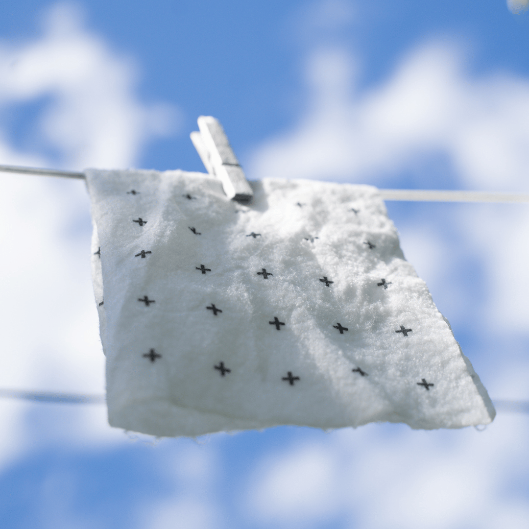 Reusable bamboo towel with black crosses hanging on a clothesline against a blue sky.