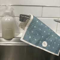 Blue eco cleaning cloth with white patterns hanging over a sink next to a handwash bottle labeled 'Cleanery'.