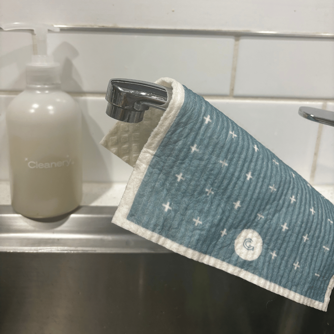 Blue eco cleaning cloth with white patterns hanging over a sink next to a handwash bottle labeled 'Cleanery'.