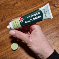 Hand applying manuka ouch balm to a small cut on a wooden surface