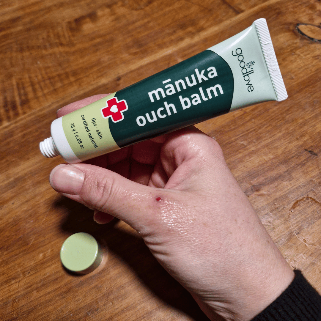 Hand applying manuka ouch balm to a small cut on a wooden surface