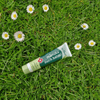 Manuka Ouch Balm tube on grass with daisies
