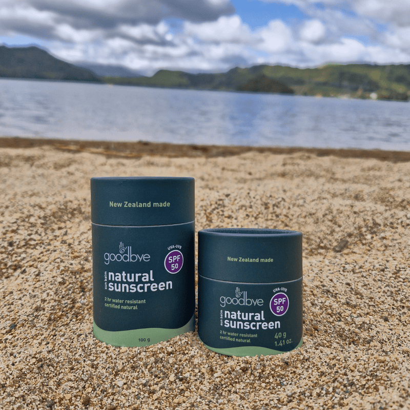 Two bottles of 'goodbye' natural sunscreen on a beach with a scenic background.