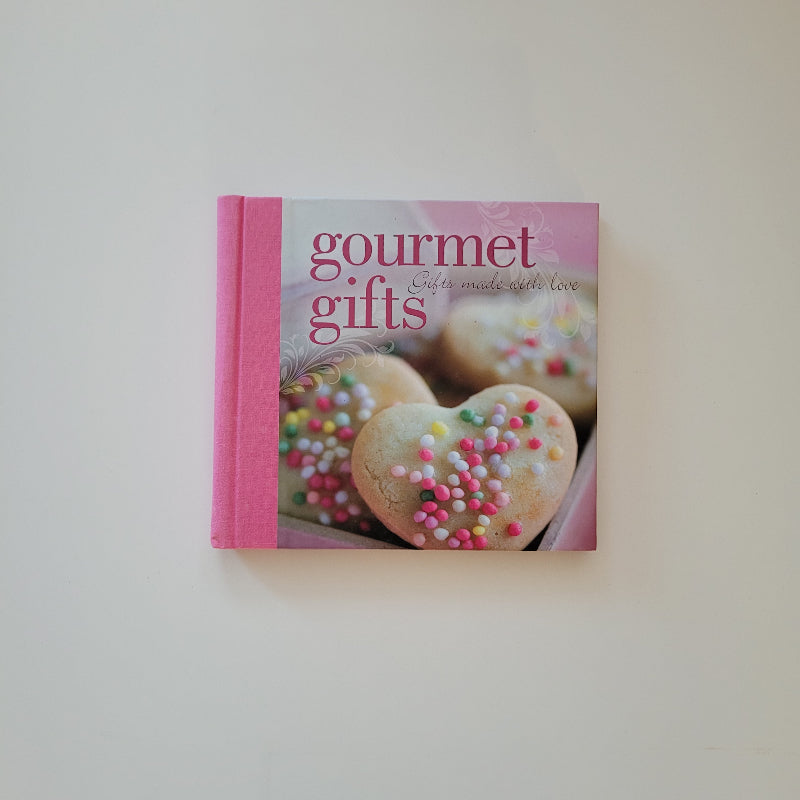 A hardcover book titled 'gourmet gifts' with a pink cover featuring a photo of heart-shaped cookies with colorful sprinkles, set against a plain off-white background.