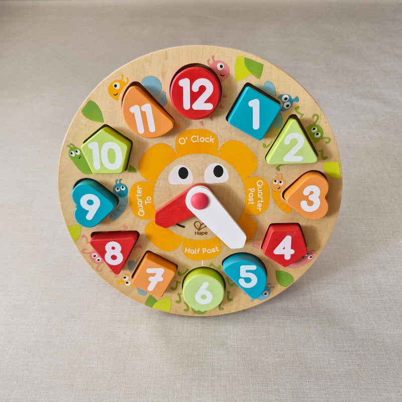 Colourful wooden clock toy with numbered and time-related pieces on a beige background