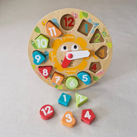 Wooden educational clock with colourful shapes and numbers on a light grey background