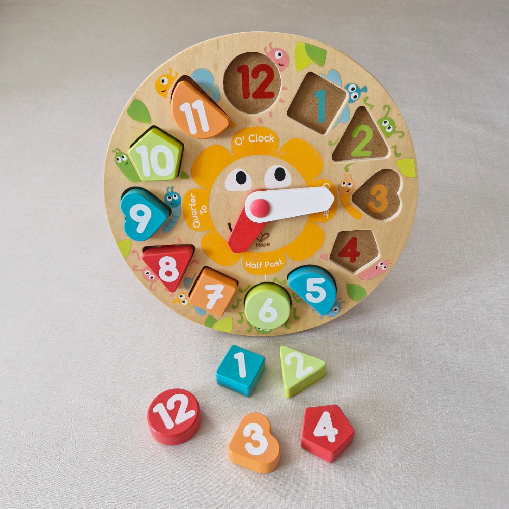 Wooden educational clock with colourful shapes and numbers on a light grey background