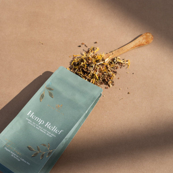 A spoonful of dried herbal mix from the product 'Hemp Relief' is shown, with a teaspoon resting on the ground beside a compostable pouch packaging.