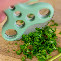 Person holding the herb stripper and using the blade to chop parsley on wooden chopping board