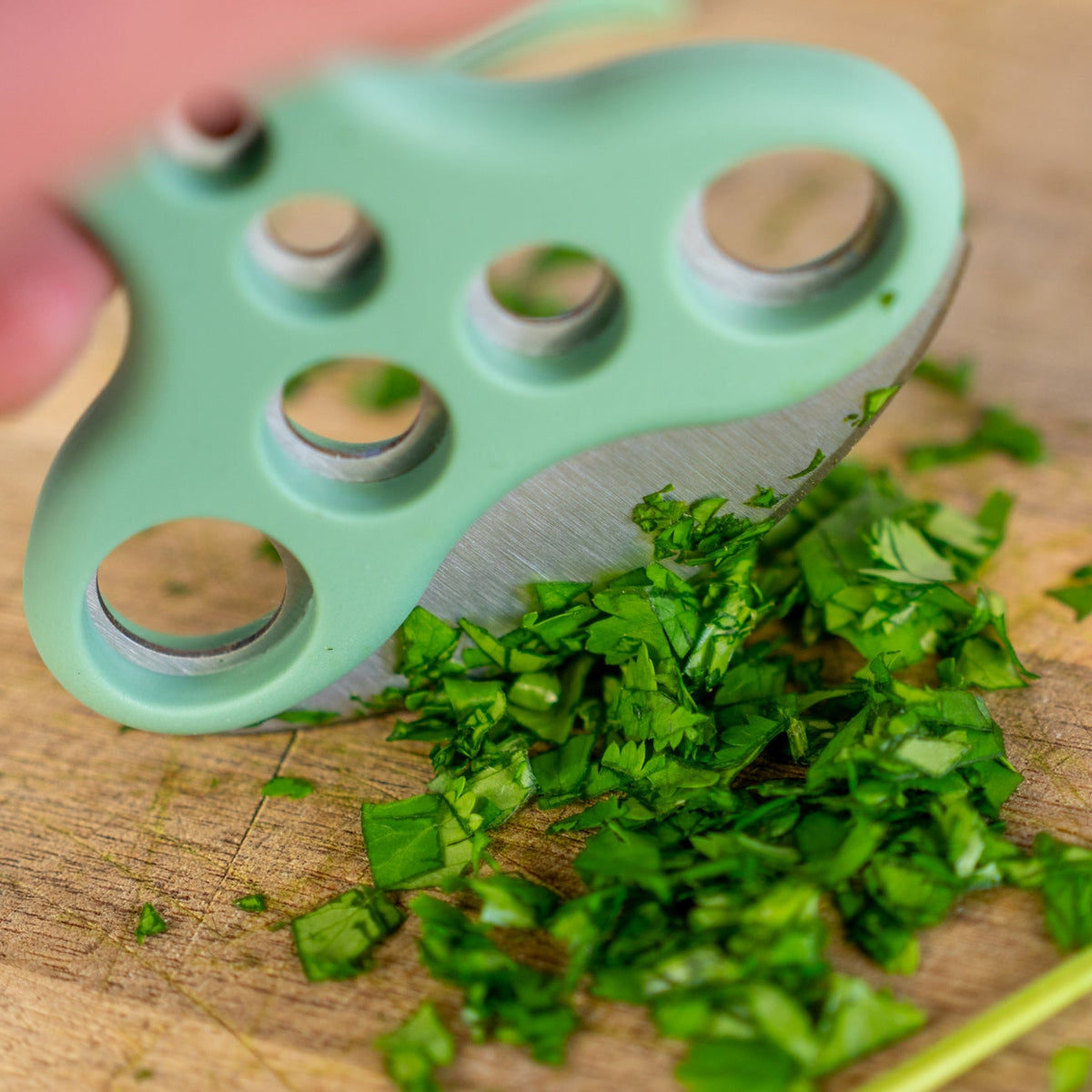 Person holding the herb stripper and using the blade to chop parsley on wooden chopping board