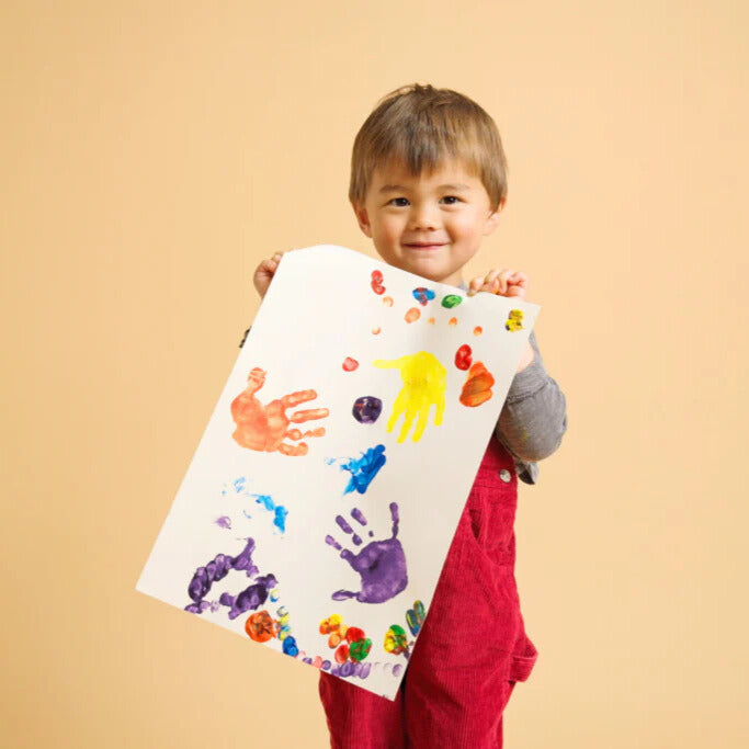 Child holding up a piece of paper showing their artwork using different paint colours