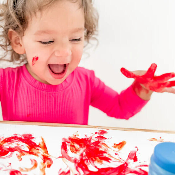 Child excited about painting with their hands using red Honeysticks finger paint