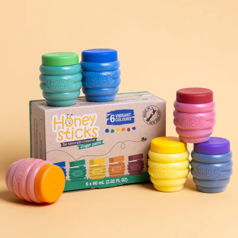 A set of Honeysticks finger paints in various colors, including blue, green, red, purple, orange, and yellow, displayed next to their packaging box.