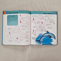 Open book showing instructions to draw dolphins on a textured surface