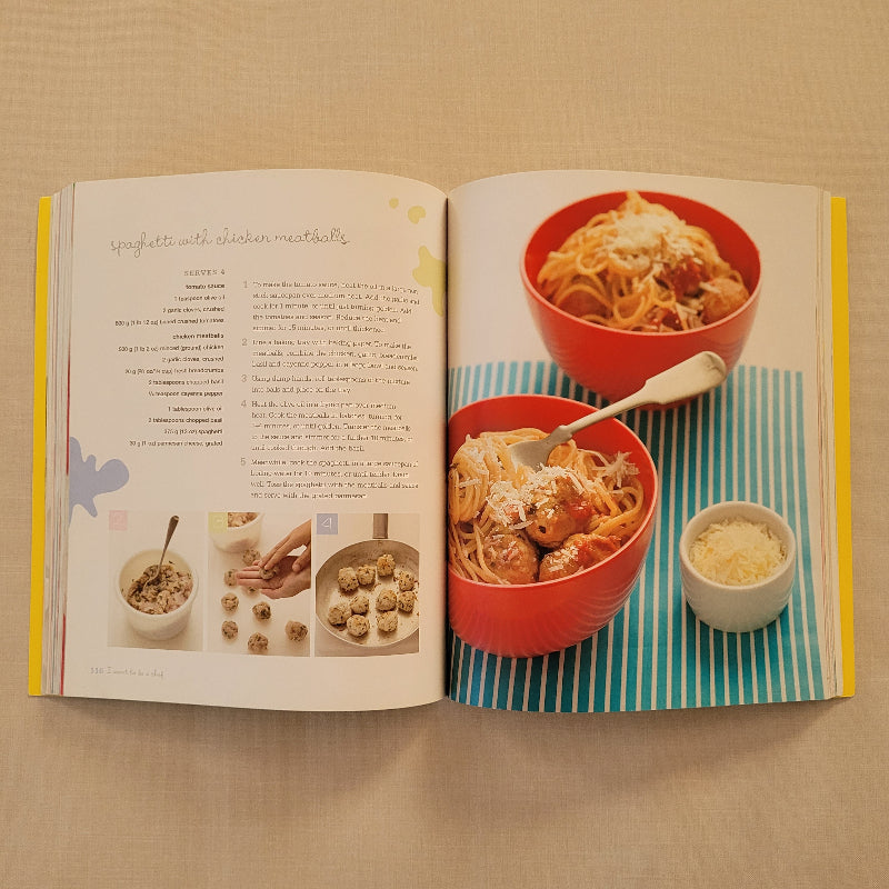An open cookbook spread showing a recipe page with photos of pasta dishes, bowls of food, and instructional text, photographed from above on a beige fabric surface.