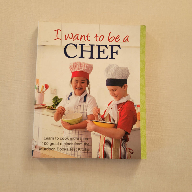A children's cookbook titled 'I want to be a CHEF' resting on a light beige textured surface. The cover features a photo of two children in chef hats and aprons mixing ingredients in a kitchen.