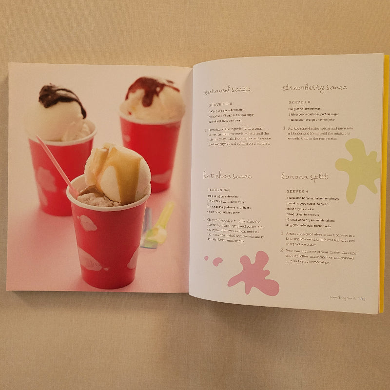 An open printed recipe book showing  a close-up photo of red paper cups filled with a creamy ice cream dessert and sauce recipes.