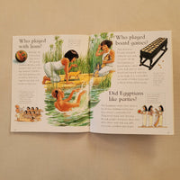 An open vintage children's book spread, photographed flat on a light beige surface. The pages feature colorful illustrations of ancient Egyptian scenes, including figures by a river, a black harp, and text headings such as 'Who played board games?' and 'Did Egyptians like portraits?'.