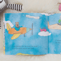 Open book with a colourful illustration of a bear on an airplane, surrounded by clouds and another airplane.