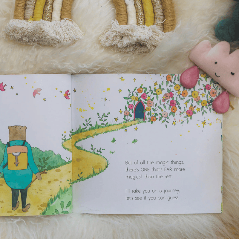 Open children's book with a colourful illustration of a bear and a house, on a soft surface.