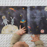 Open book with space-themed illustrations and a child's hands on a textured surface