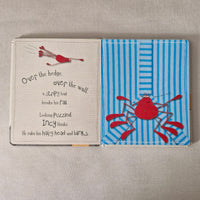 Childrens book with a red spider illustration on a blue striped cover, placed on a textured surface.