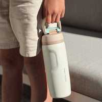 Person holding a cream water bottle with a handle in a casual setting