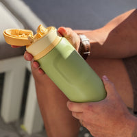 Person holding a green water bottle with a yellow cap outdoors