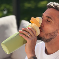 Man drinking from a green and yellow water bottle with a blurred outdoor background