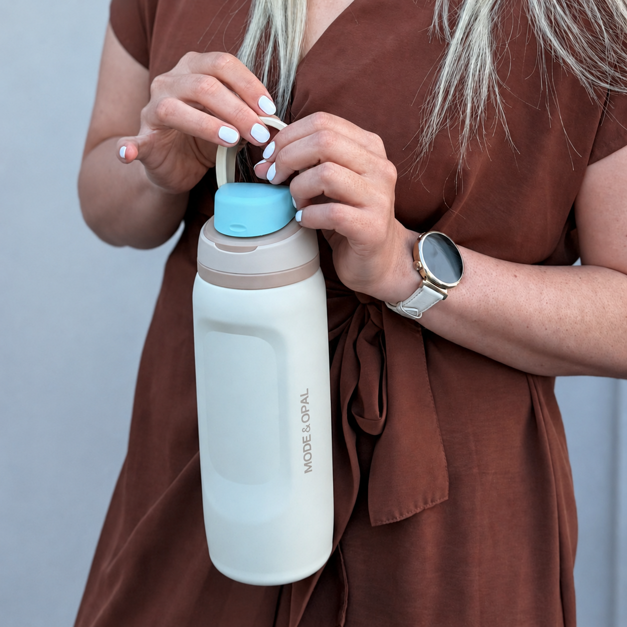 Person holding a white water bottle with a blue cap against a neutral background