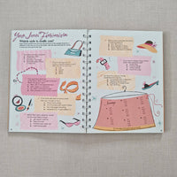 Open spiral-bound book page with colourful fashion pages on a textured surface