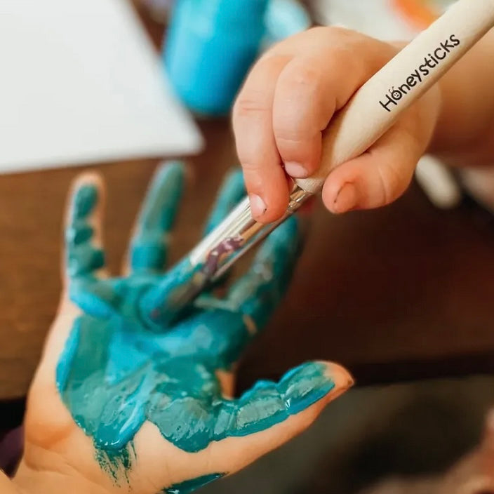 Jumbo paint brush with greeny blue paint, painting a childs hand
