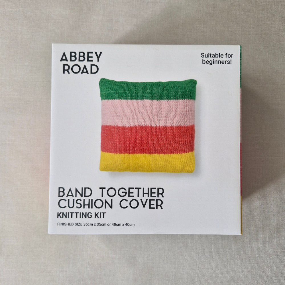 Knitting kit packaging with a striped cushion cover on a beige fabric background