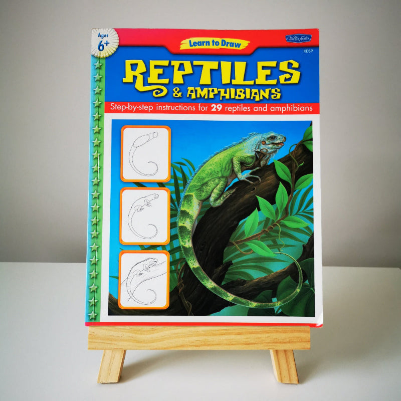 A book titled 'Learn to Draw Reptiles and Amphibians' by Walter Foster, illustrated by Diana Fisher', displayed on a small wooden easel.