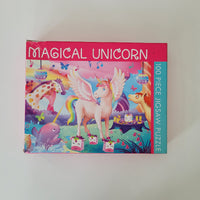 A 100-piece jigsaw puzzle box titled 'MAGICAL UNICORN' featuring a colorful illustration of a pink winged unicorn with a rainbow mane, set against a plain off-white background.