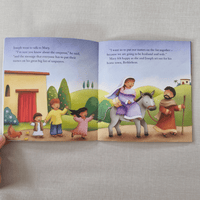 Open children's book with illustrations of a family and a donkey on a grey surface