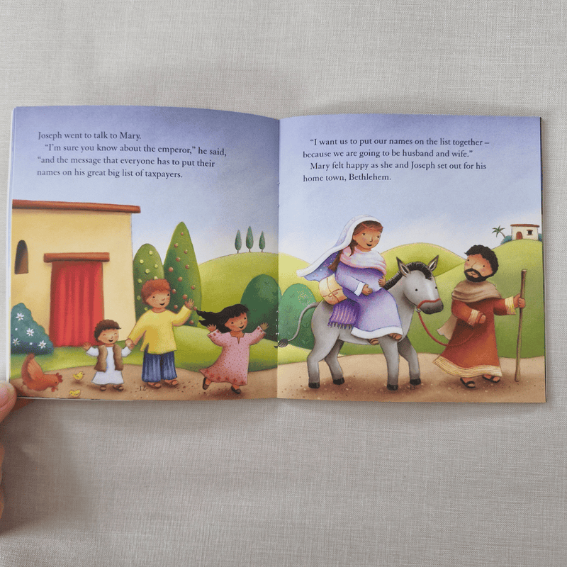 Open children's book with illustrations of a family and a donkey on a grey surface