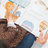 Child's hand holding a children's book with illustrations of animals and balloons.