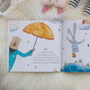 Open children's book with illustrations of a bear holding an umbrella and a rabbit in the rain, on a soft surface.