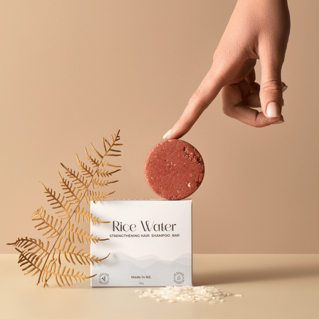 Hand holding a rice water shampoo bar with packaging on a beige background