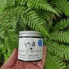 Hand holding a jar of 'Back to the Wild' natural sunscreen against a green leafy background