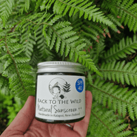 Hand holding a jar of 'Back to the Wild' natural sunscreen against a green leafy background