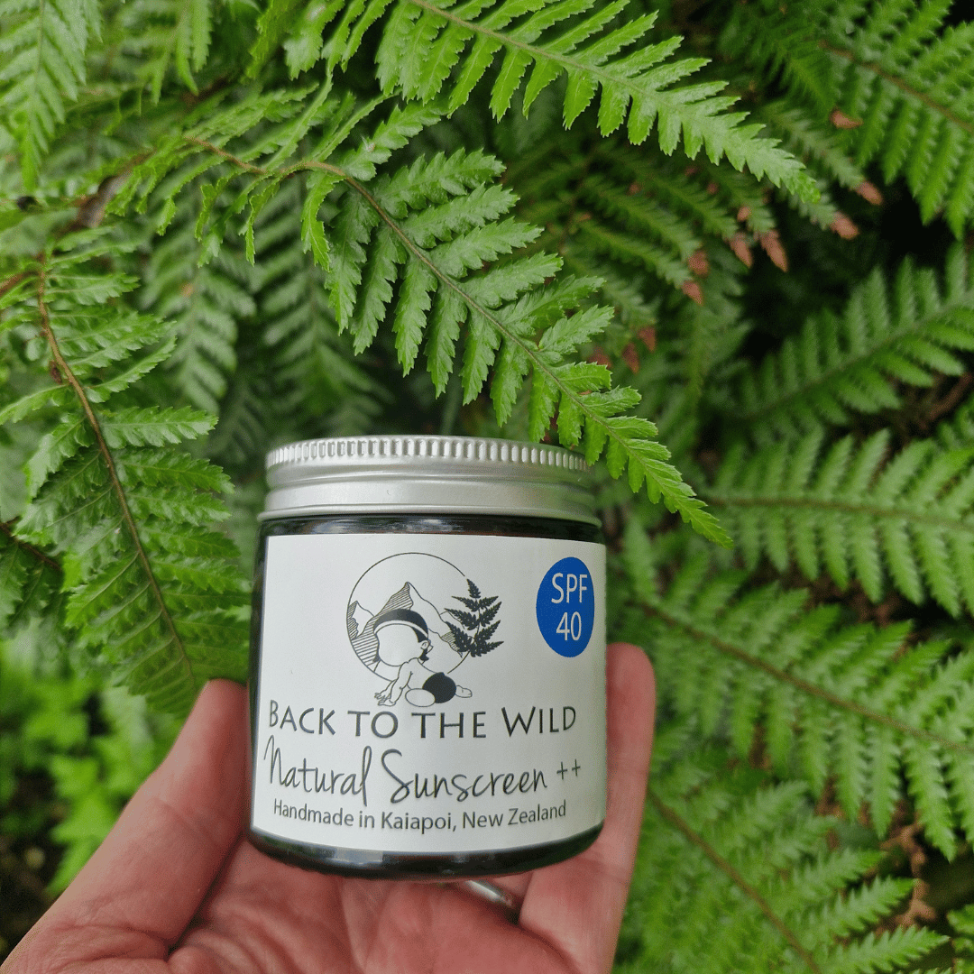 Hand holding a jar of 'Back to the Wild' natural sunscreen against a green leafy background