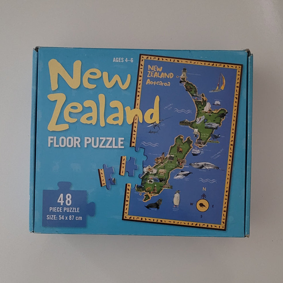 A blue box for a New Zealand floor puzzle, showing the product title, piece count, and a printed illustration of the New Zealand map on the front.
