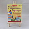Book titled 'Nonfiction Comprehension Cliffhangers' by Scholastic on a wooden stand against a grey background
