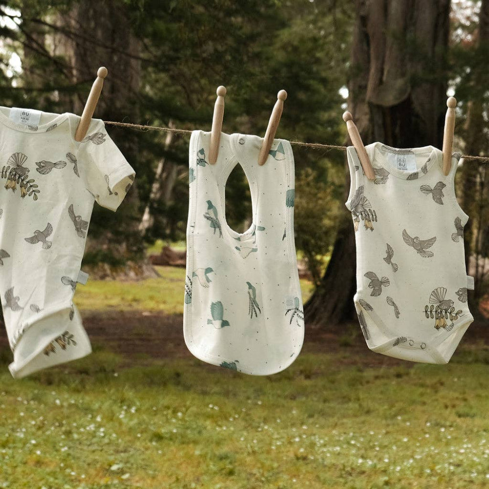 Three baby rompers with bird patterns hanging on a clothesline outdoors.